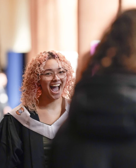 Graduate with curly pink hair smiling excitedly in graduation gown Graduate with curly pink hair smiling excitedly in graduation gown